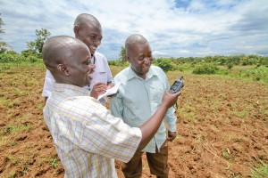 Asuman, left, measures his fields with a GPS device and help from Regional Agricultural Supervisor John Peter Emoi, center, and fellow farmer Joseph Mulandya.