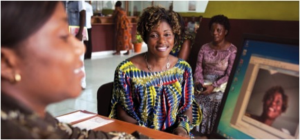 Annie Nyangomba smiles for the camera at Opportunity’s new branch in the DR Congo. Bank Teller Alma Romina takes the photo for Annie’s ID card as part of the process of opening a biometric-based account.